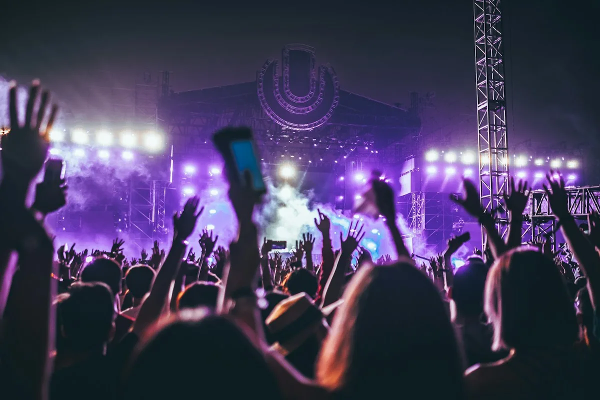 A concert crowd reaching toward a stage under purple lights